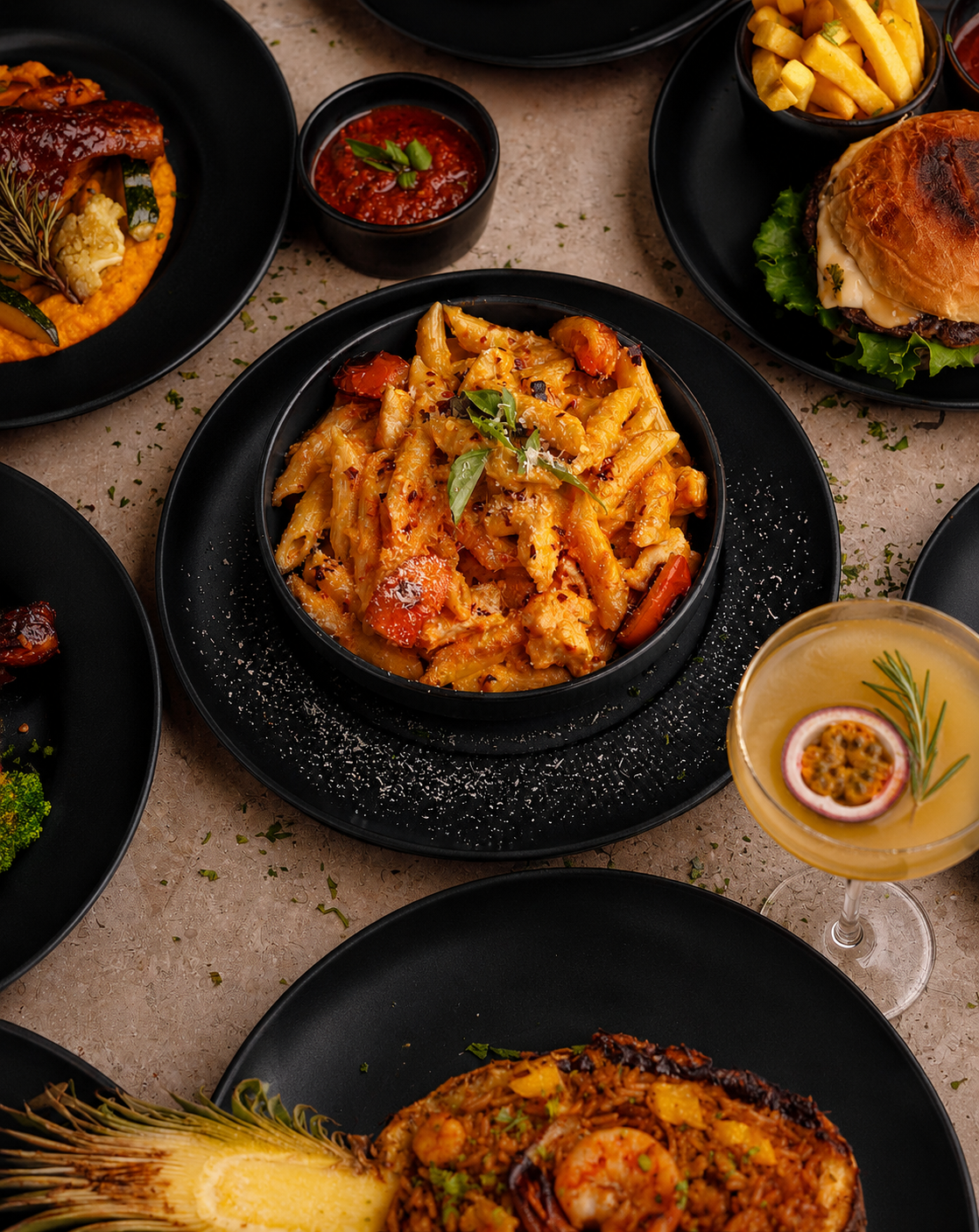 Signature penne in a rich, smoky tomato cream with charred vegetables and fresh basil, plated across a spread of black stoneware.